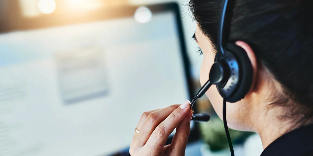 Close-up from behind of a team member wearing a headset at a computer workstation.