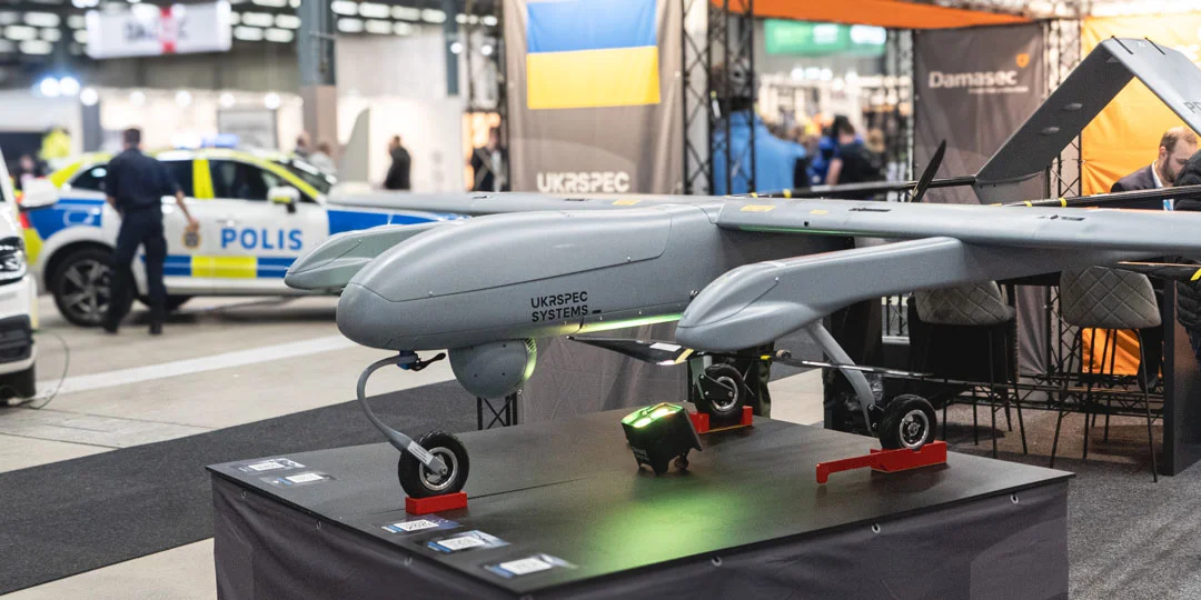 Drone displayed at SKYDD with a police vehicle and exhibition stands in the background.<br>