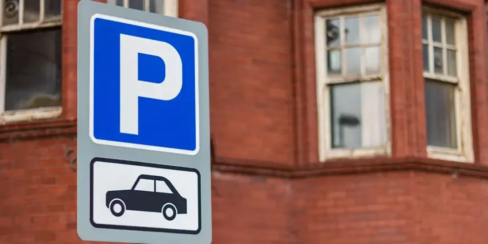 Skylt som visar parkering för bilar framför en tegelbyggnad.