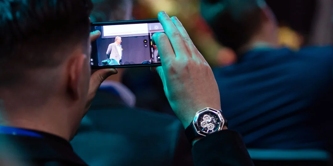 Visitors filming a speaker on stage during an event at Stockholmsmässan.