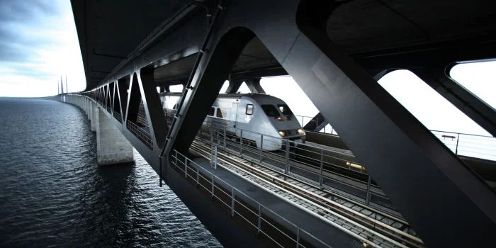 Snabbtåg som kör över en bro med vatten under och stålkonstruktion runt spåren.