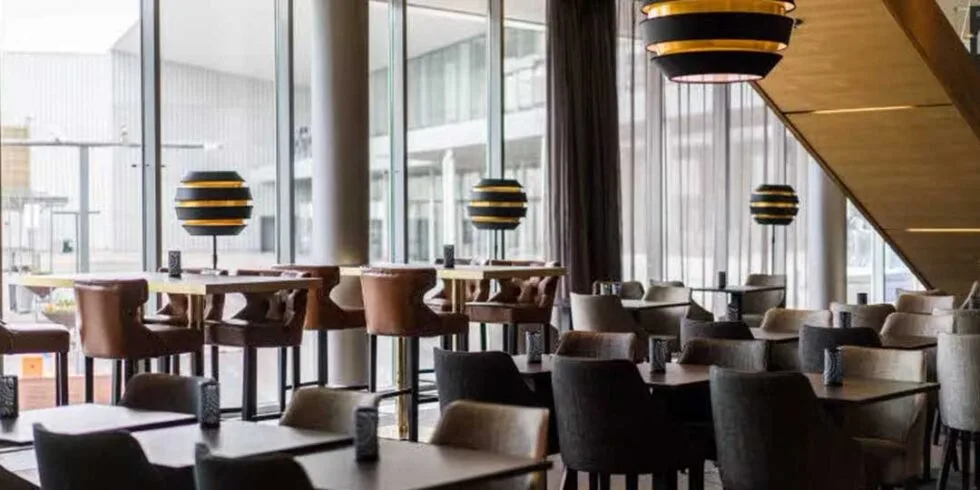 Restaurangmiljö med bord och stolar inne i lobbyn på Sacndic Talk, med stora fönster och dagsljus.